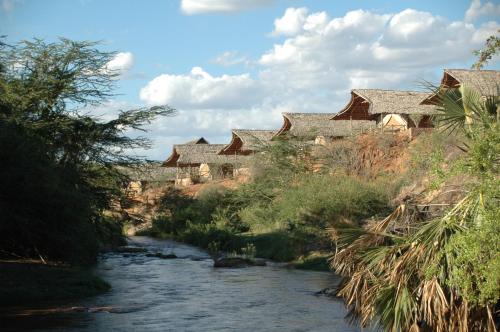a river with a group of houses in the background at Maneaters in Tsavo