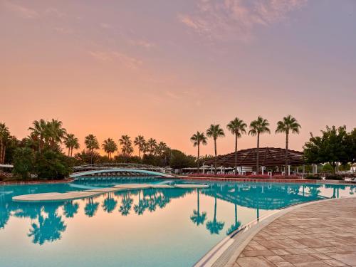 a pool with palm trees and a sunset in the background at Lara Barut Collection-Ultra All Inclusive in Lara