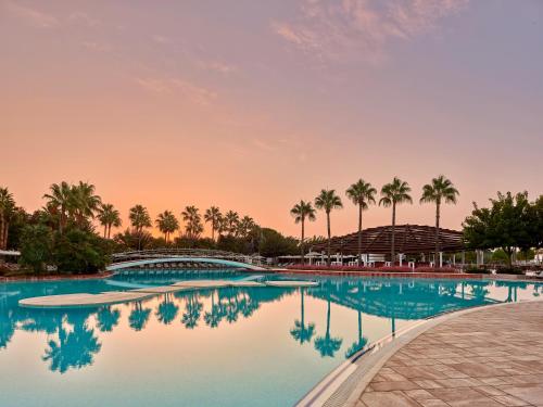 einem Pool mit Palmen und einem Sonnenuntergang im Hintergrund in der Unterkunft Lara Barut Collection-Ultra All Inclusive in Lara