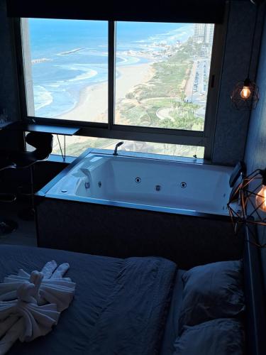 a bedroom with a large window and a bath tub at מלון כרמל/מגדל C in Netanya