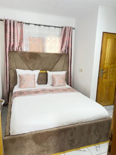 a bed with white sheets and pink pillows in a room at Chambre moderne avec cuisine à Bonamoussadi (Kotto) in Douala
