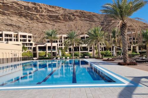 a large swimming pool with palm trees and buildings at One Bedroom Apartment Muscat Bay in Muscat