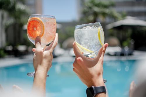 a person holding up two cocktails in front of a pool at Holiday Inn Rosario by IHG in Rosario