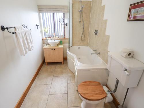 a bathroom with a tub and a toilet and a sink at Tawny Cottage in Alford