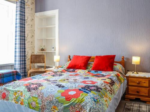 a bedroom with a colorful bed with red pillows at Kirk Wynd Cottage in Kirriemuir