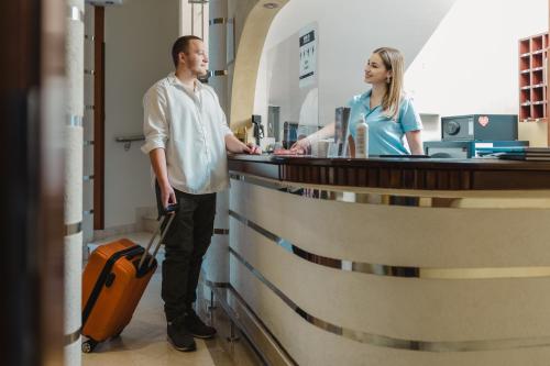 a man and a woman standing at a counter with a suitcase at Garni Hotel Koral in Budva