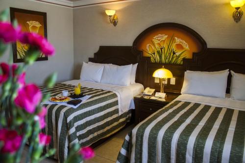 a hotel room with two beds and a table with flowers at Hotel Casino Plaza in Guadalajara
