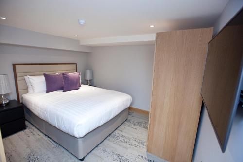 a bedroom with a bed with white sheets and purple pillows at Sanctum Belsize Road in London