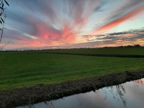 a sunset over a field with a river at B&B De Verre Kijker in Barsingerhorn