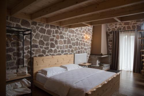 1 dormitorio con 1 cama grande y pared de piedra en George Boutique Hotel, en Voskopojë