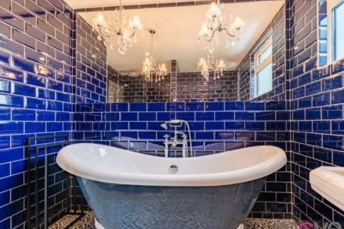 La salle de bains est pourvue de carrelage bleu, d'une baignoire et d'un lavabo. dans l'établissement Modern 4 bed home, hottub and traditional pub, à Down Hatherley