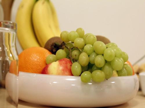 a bowl of fruit with grapes apples oranges and bananas at KEF Guesthouse by Keflavík airport in Keflavík