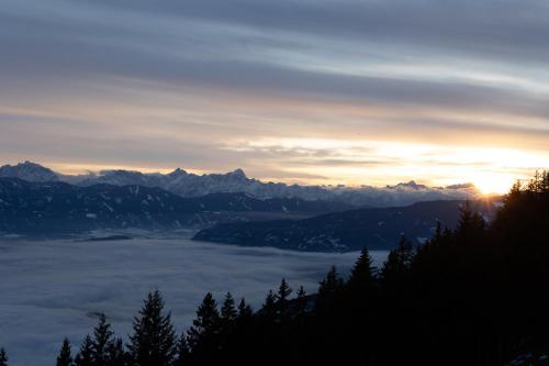 a view of a mountain range with the sun setting over the clouds at L&P Appartement Gerlitzen & Pool - Haus Enzian in Kanzelhöhe