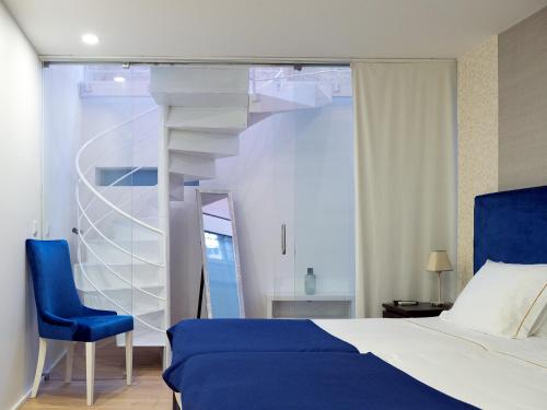 a bedroom with a bed and a blue chair and a spiral staircase at Apartamentos Premium Familiares - Loft Guesthouse BeMyGuest Viseu in Viseu