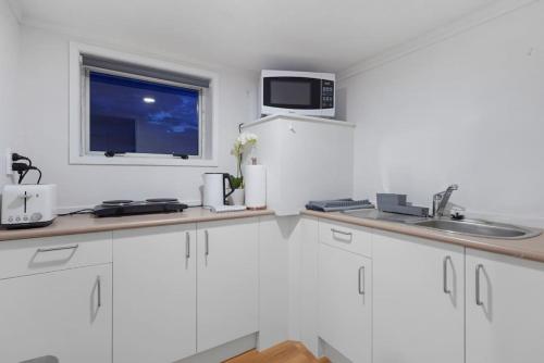 a white kitchen with a sink and a window at The Nifty Nook Studio with Parking and Wi-fi in Auckland