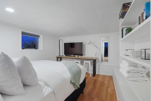 a white bedroom with a bed and a television at The Nifty Nook Studio with Parking and Wi-fi in Auckland