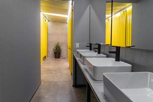 une rangée de lavabos dans une salle de bains avec des lumières jaunes dans l'établissement CHECK INN HOSTAL AEROPUERTO GDL, à Guadalajara