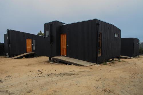 un edificio negro con puertas marrones en un campo de tierra en Cabaña para dos personas en Punta de Lobos PUERTO LA MAR, en Pichilemu