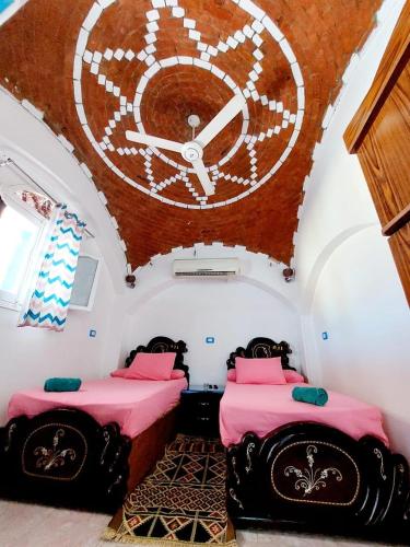 two beds in a room with a large clock on the wall at Gamal Robob Nubian Guest House in Aswan