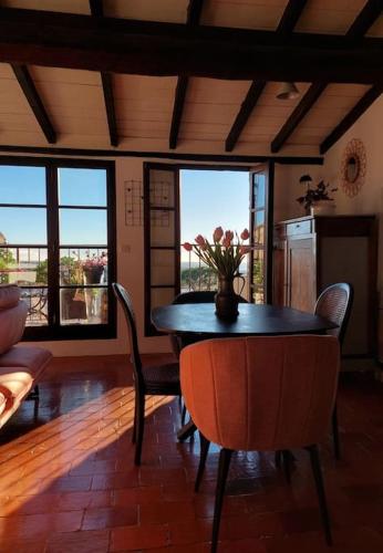 une salle à manger avec une table, des chaises et des fenêtres dans l'établissement Maison de village Haut-de-Cagnes avec vue mer, à Cagnes-sur-Mer