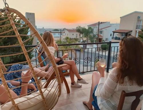 three women sitting in a hammock on a balcony with wine glasses at EMPA SUNSET VIEWS VILLA in Emba