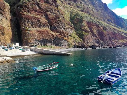 two boats in a body of water next to a mountain at Casa da Rocha in Paul do Mar