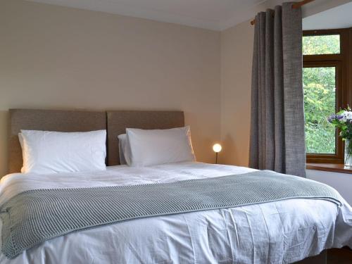 um quarto com uma cama com lençóis brancos e uma janela em Rowan House em Glencripesdale