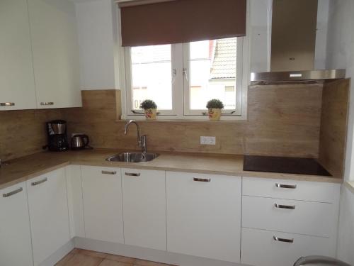 a kitchen with white cabinets and a sink and two windows at Holiday Home in Quiet Park for Families in Wemeldinge