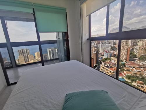 sypialnia z białym łóżkiem i dużymi oknami w obiekcie APTO SM MONTECARLO P19 EDIF.GEMELOS 15 BENIDORM PLAYA LEVANTE w mieście Benidorm