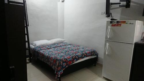 Habitación pequeña con cama junto a una nevera. en Apartasuites Medellin Laureles Nogal, en Medellín