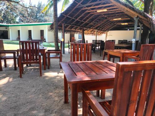 a group of wooden tables and chairs under a pavilion at Hotel Coral Bay in Trincomalee