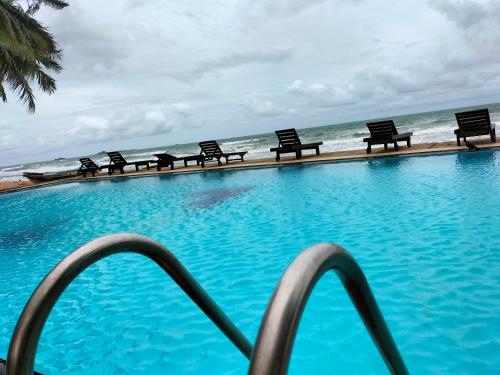 a swimming pool with benches in front of the ocean at Hotel Coral Bay in Trincomalee