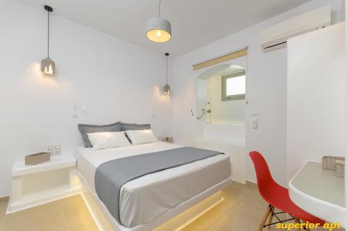 a white bedroom with a bed and a red chair at Aphrodite Luxury Apartments in Agios Prokopios