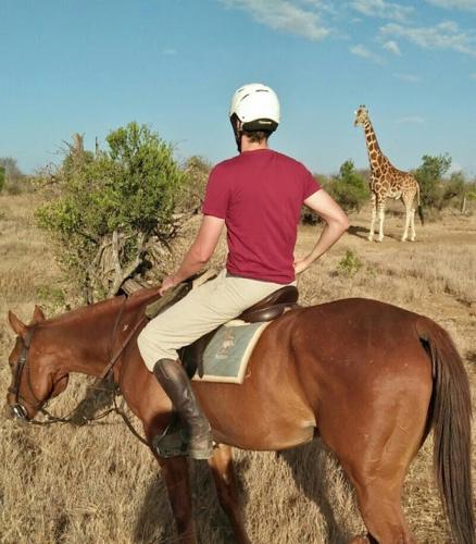 a man riding a horse with a giraffe in the background at Mount Kenya Farm Stay in Nanyuki