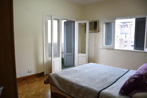 a bedroom with a bed and two windows and a balcony at Agouza NileView Apartment in Cairo