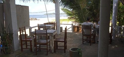 a man sitting at a table in a restaurant overlooking the beach at Gems Garden Guest House in Tangalle