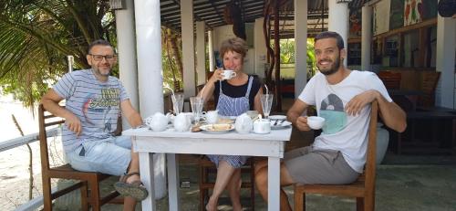 three people sitting at a table drinking coffee at Gems Garden Guest House in Tangalle