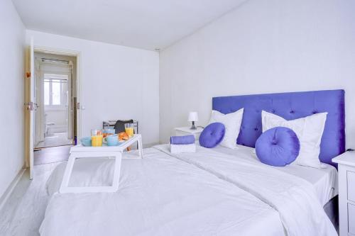 a white bedroom with a large bed with purple pillows at My Cosy Home 1 in Vitry-sur-Seine