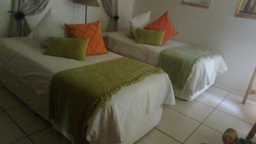 two beds in a room with orange and green pillows at Harmony Guesthouse in Nelspruit