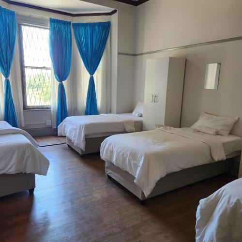 3 camas en una habitación con cortinas azules en Msunduzi River View backpackers, en Pietermaritzburg