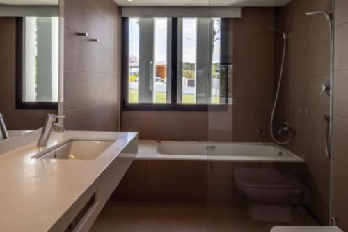 baño con bañera, lavabo y ventana en Camiral Golf and Wellness Luxury Villa, en Girona