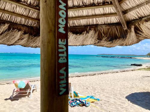 a beach with a straw umbrella and a chair and the ocean at BlueMoon Villa - Authentic, seaside living in Trou dʼ Eau Douce