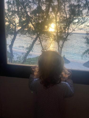a little girl looking out a window at the water at BlueMoon Villa - Authentic, seaside living in Trou dʼ Eau Douce