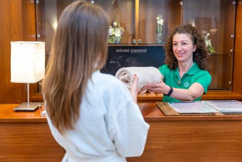 a woman standing at a counter talking to a girl at Tisza Balneum Hotel in Tiszafüred