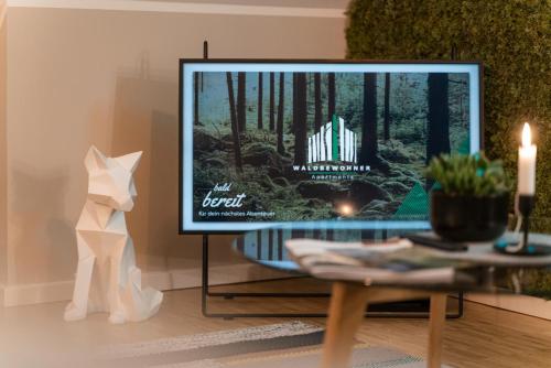 a television in a living room with a cat and a table at Waldbewohner Apartments / Fuchs in Ilsenburg