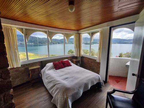 a bedroom with windows and a bed with a view of the water at Refugio Génesis habitaciones Lago de Tota in Tota