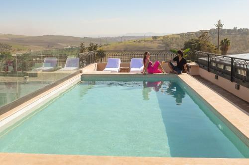 dwie kobiety siedzące obok basenu w obiekcie DAR LYS w Fezie
