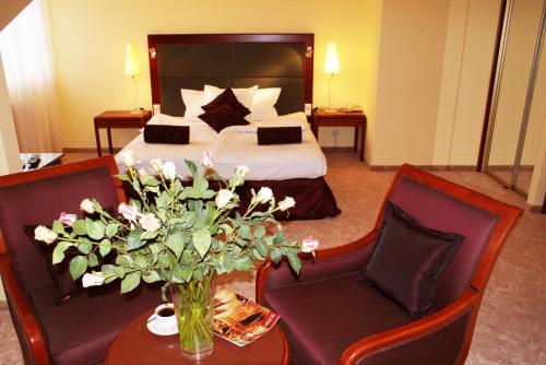 a hotel room with a bed and two chairs and a table with flowers at Hotel Wilga by Katowice Airport in Pyrzowice