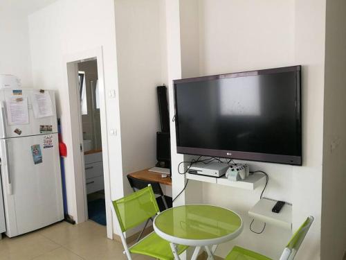 a flat screen tv hanging on a wall with a table and green chairs at Charming unit in Dead Sea in Ovnat