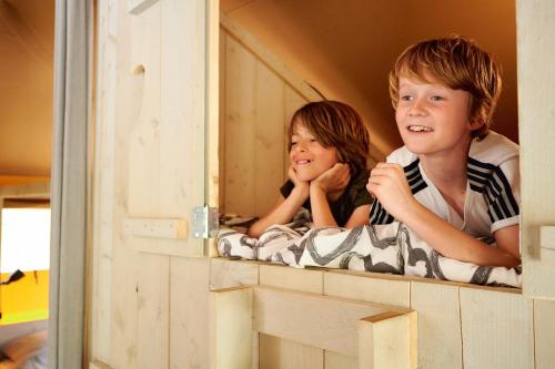 two children are looking out of a play house at Camping Vossenberg - op de Veluwe! in Epe